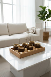High Objects EMBERFORM glass cup set of 6, amber-tinted glass with wooden grip sleeves, on a wooden tray.