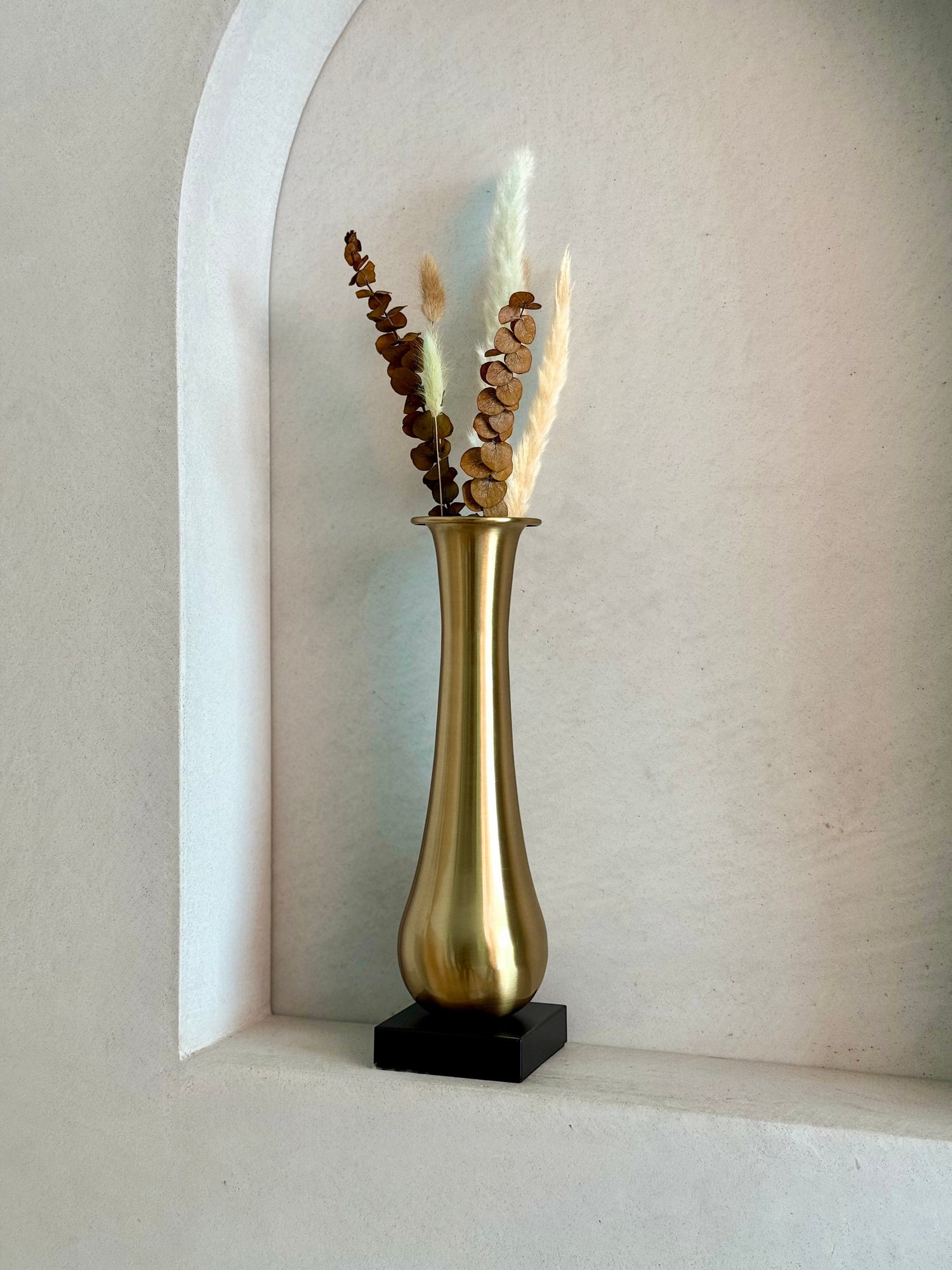 High Objects Eterna Gold Vase with a sleek silhouette and black square base, holding dried eucalyptus and pampas grass.