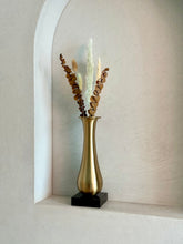 High Objects Eterna Gold Vase with a sleek silhouette and black square base, holding dried eucalyptus and pampas grass.