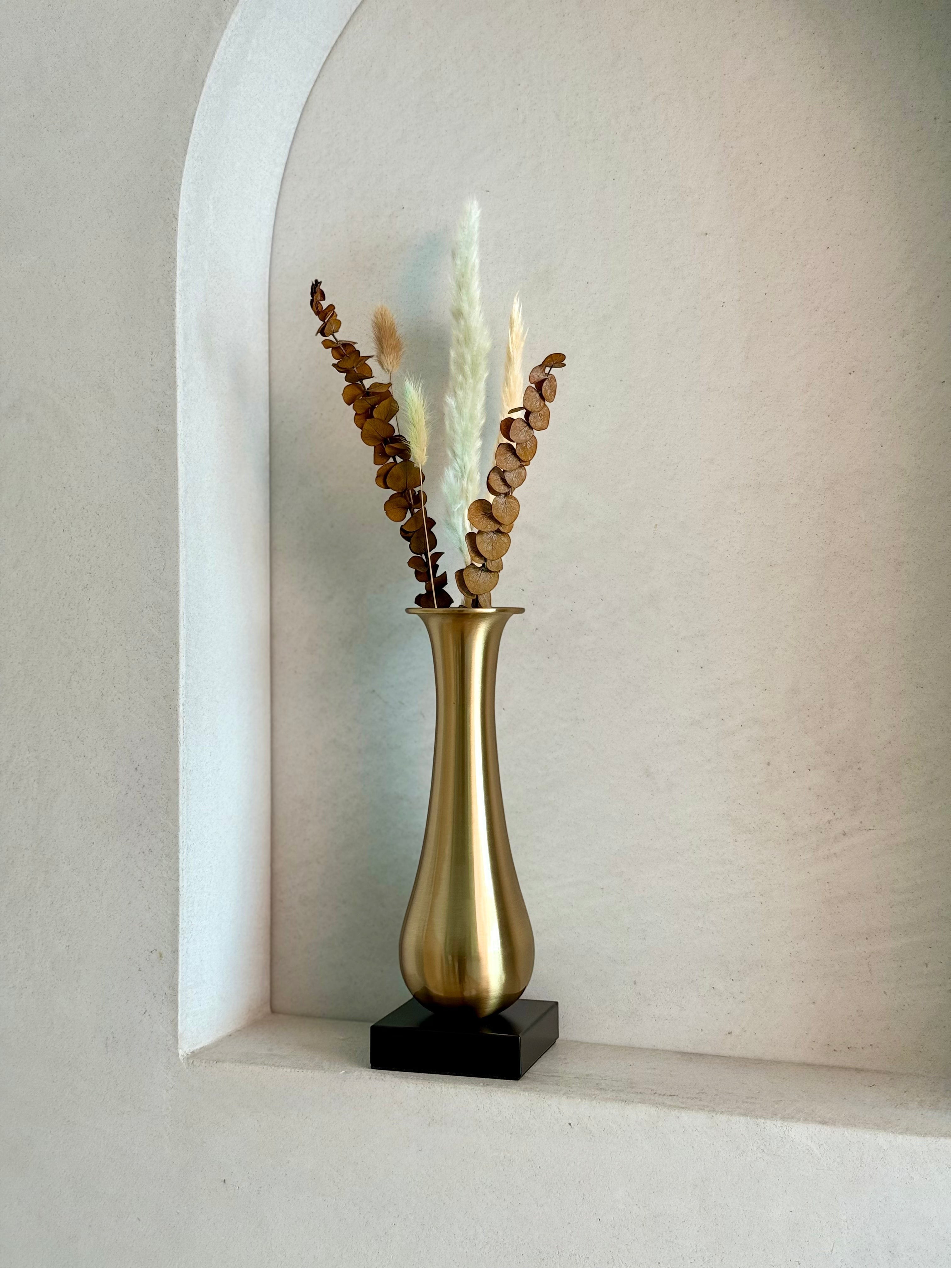 High Objects Eterna Gold Vase with a sleek silhouette and black square base, holding dried eucalyptus and pampas grass.