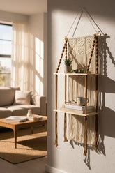 High Objects Ethereal Wall Harmony Shelf, a macrame hanging shelf with two wooden shelves, cream cotton rope, and brown accents. Holds books, mug, and plant.