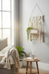 High Objects Ethos Boho Wall Shelf with macrame detailing, wooden shelf, and tassels. Holds books and a plant.