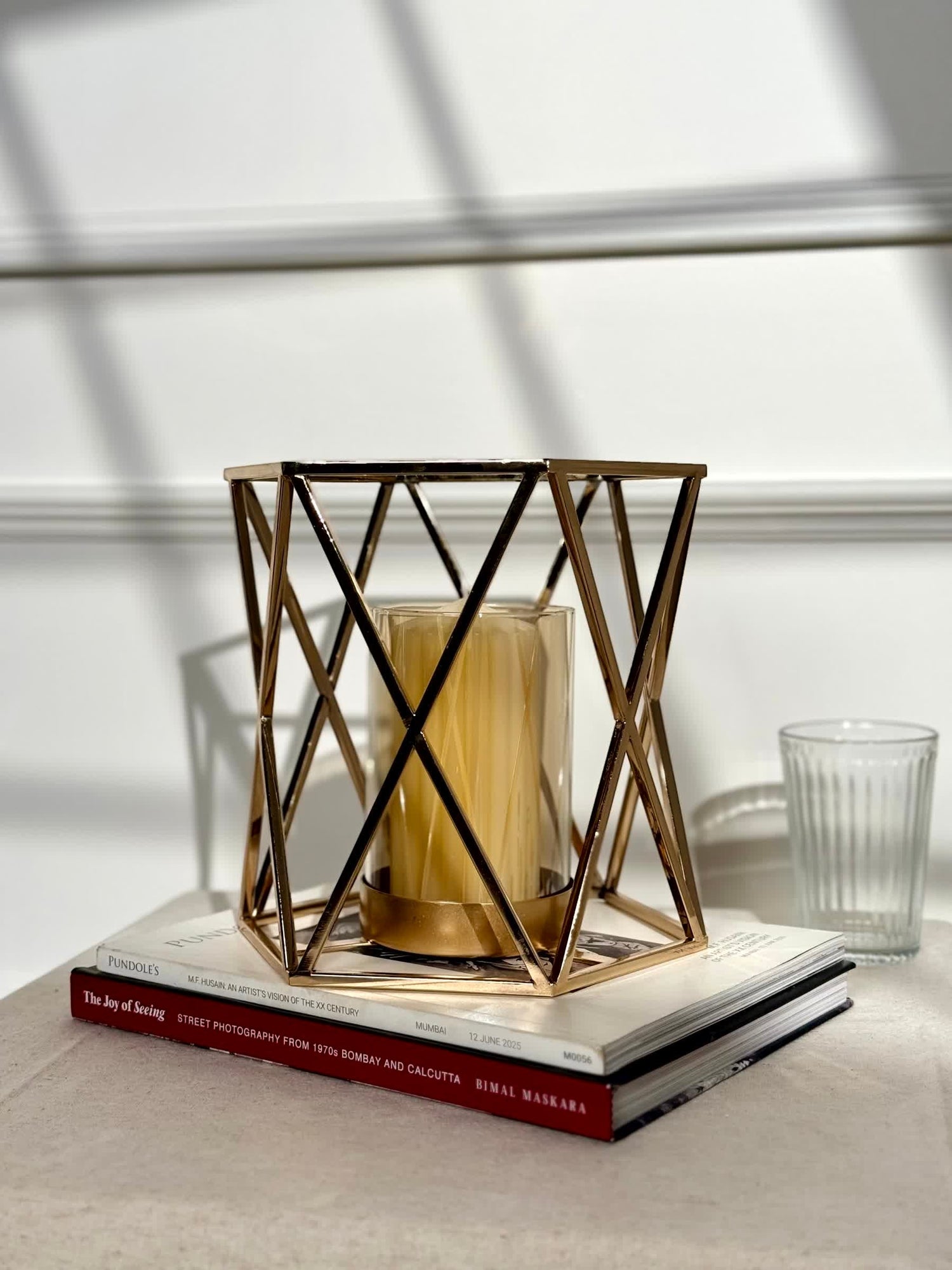 High Objects Gilded Prism Candle Stand with gold geometric frame and glass holder, holding a yellow candle.