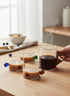 High Objects glass cup bundle featuring four beaker-style cups with colored glass handles and one mug with a wooden handle, filled with coffee.