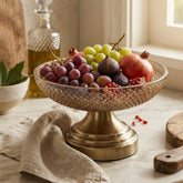 High Objects ornate glass pedestal fruit bowl filled with grapes, figs, and pomegranates on a marble countertop.