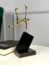 High Objects Golden Balance Artefact, abstract metal sculpture of a figure balancing on a tilted black block.