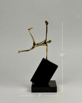 High Objects Golden Balance Artefact, abstract metal sculpture of a figure balancing on a tilted black block.