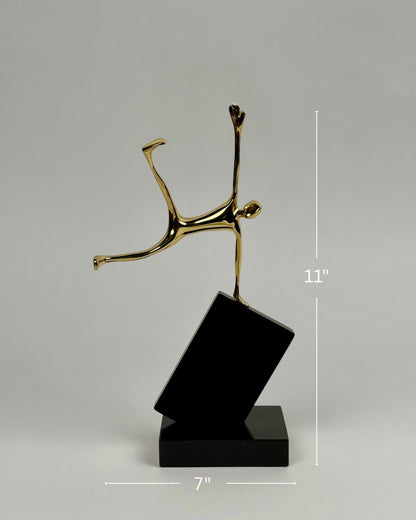 High Objects Golden Balance Artefact, abstract metal sculpture of a figure balancing on a tilted black block.