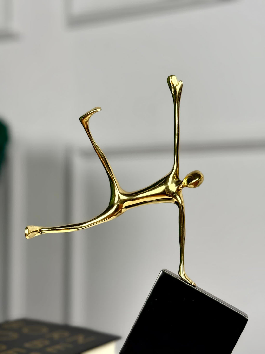 High Objects Golden Balance Artefact, abstract metal sculpture of a human figure balancing on a tilted black block.