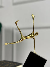 High Objects Golden Balance Artefact, abstract metal sculpture of a human figure balancing on a tilted black block.