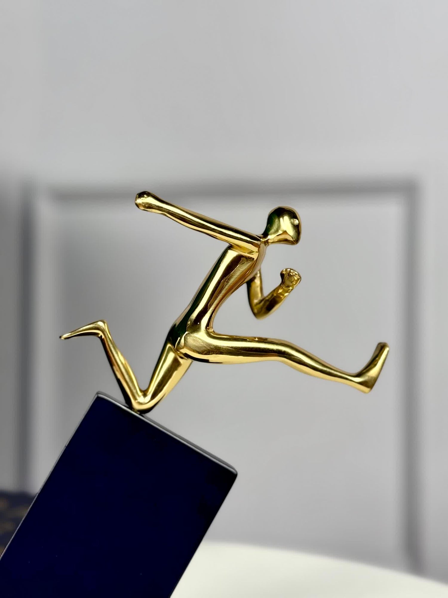 High Objects polished gold hurdler leaping over a black pedestal, symbol of ambition and momentum.