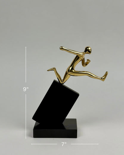 High Objects Golden Hurdler Leap Artefact sculpture, polished gold figure mid-flight on a black angled pedestal.