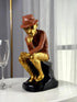 High Objects Golden Thinker Showpiece, a polyresin monkey in a gold suit and brown fedora, in a thoughtful pose on a black base.