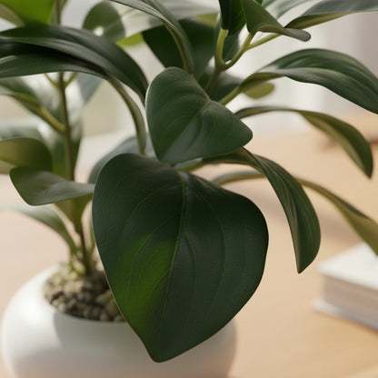 High Objects green artificial plant in a white ceramic pot with pebbles, on a wooden desk with a book and glasses.
