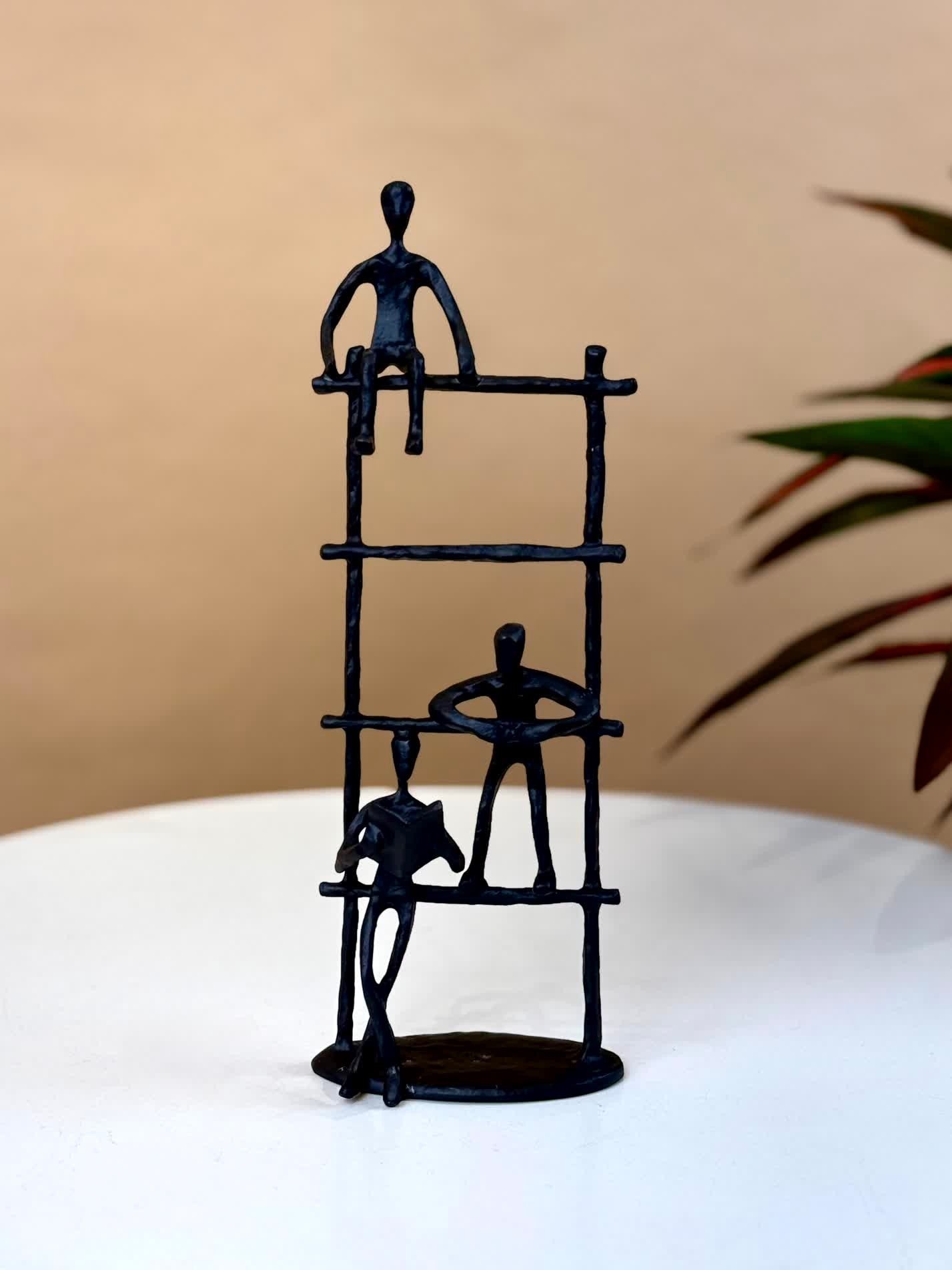 High Objects Journey Ladder Artefact, matte black iron sculpture with three abstract figures climbing a ladder, symbolizing progress and teamwork.