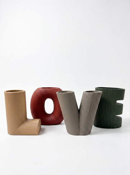 High Objects set of four decorative vases in the shape of the letters L, O, V, and E. Colors include tan, deep red, grey, and forest green.