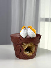 High Objects rustic cracked pot planter with two yellow and white lovebirds perched on the rim and a nest with eggs inside.