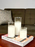 High Objects Lumiglass LED Candle Collection, set of 3 white pillar candles in glass cylinders on magazines.