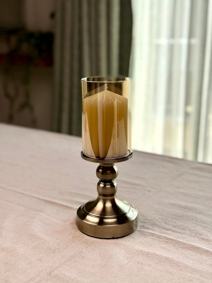 High Objects Luminaria Pedestal Candle Stand Set with tinted glass hurricane and metallic stem, holding a yellow candle.