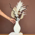 High Objects Lunara Vase, a white ribbed ceramic vase with a dried floral arrangement. Features pampas grass, palm leaves, and lotus pods.