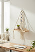 High Objects natural cream macramé hanging shelf with wooden board, blue evil eye details, holding books and a cup.