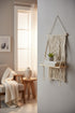 High Objects cream macramé shelf with diamond and chevron weaves, natural wood base, holding books and a plant.