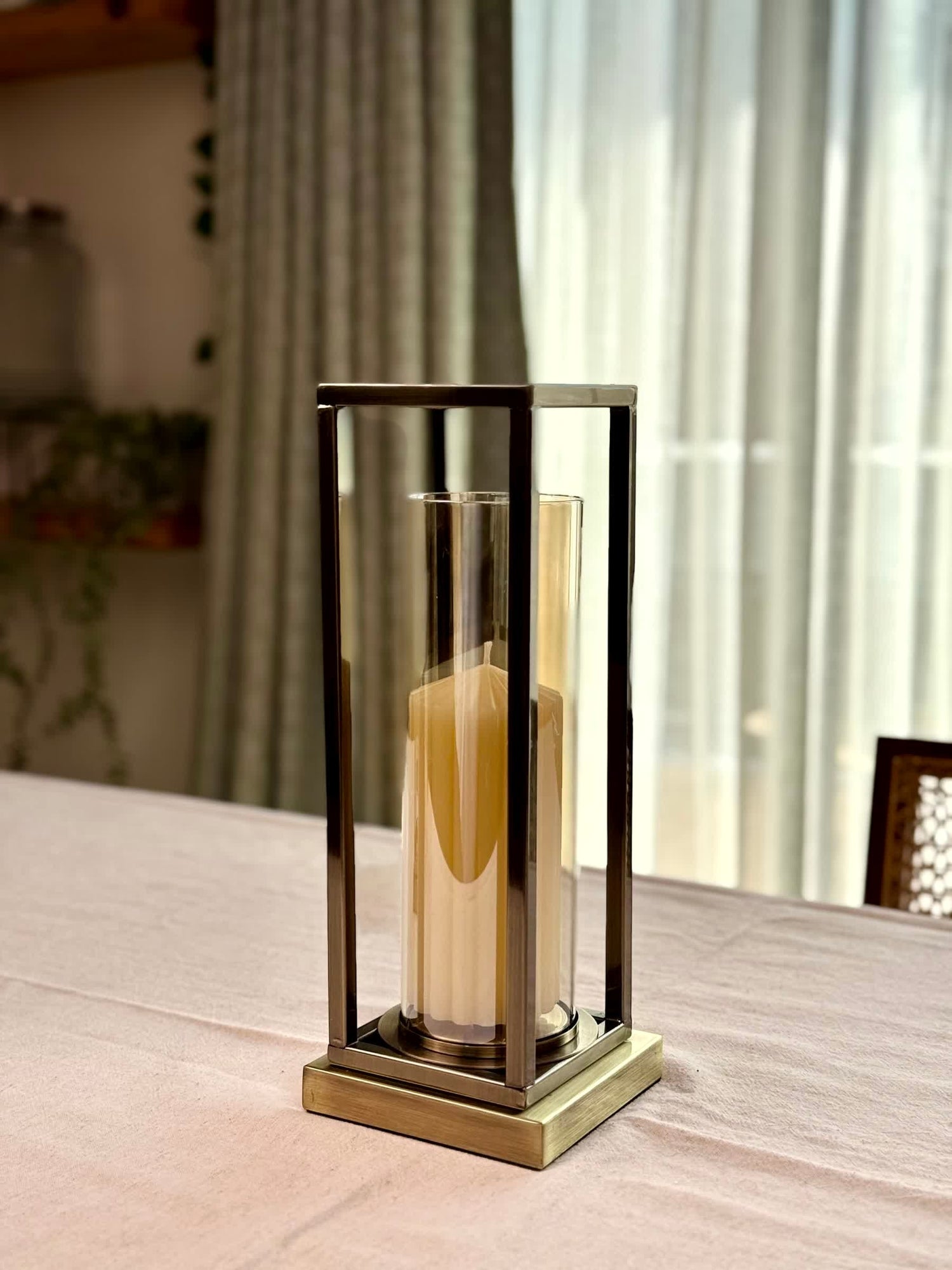High Objects Modern Halo Frame Candle Stand Set with a tall pillar candle inside a cylindrical glass holder, set on a table.