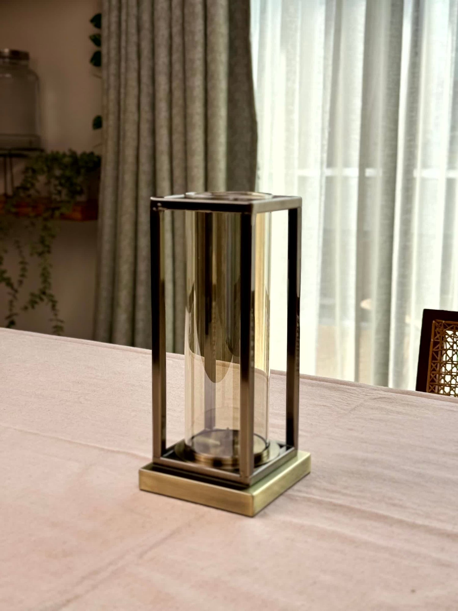 High Objects Modern Halo Frame candle stand with bronze metal frame and glass cylinder on a pink tablecloth.
