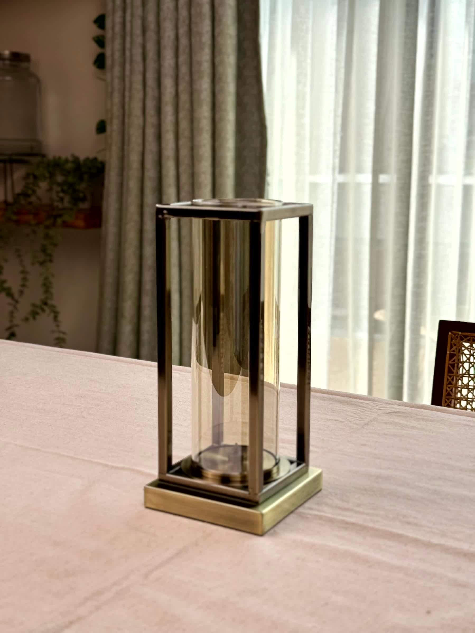 High Objects Modern Halo Frame candle stand with bronze metal frame and glass cylinder on a pink tablecloth.
