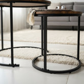 High Objects modern nesting coffee table set with round wood tops and black metal frames. One table holds books and a plant, the other a tablet and glasses.