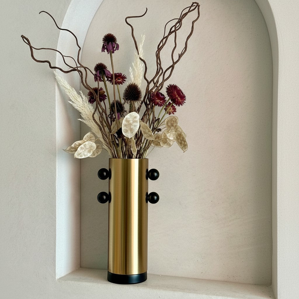 High Objects Orbis Luxe cylindrical gold vase with black orb accents, holding dried flowers.