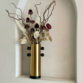 High Objects Orbis Luxe cylindrical gold vase with black orb accents, holding dried flowers.