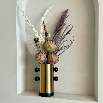 High Objects Orbis Luxe cylindrical gold vase with black orb accents and dried floral arrangement.