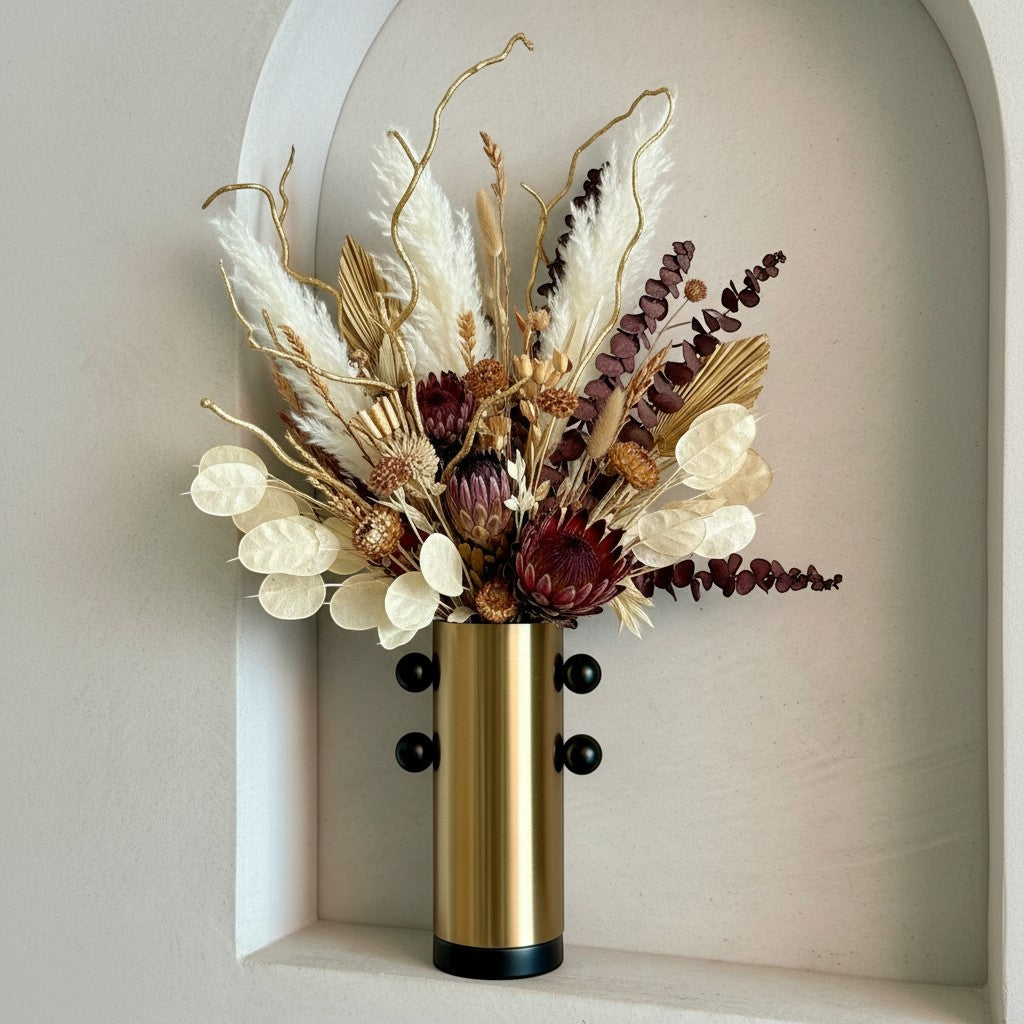 High Objects Orbis Luxe Vase: Cylindrical gold vase with black orb accents, holding a dried floral arrangement.