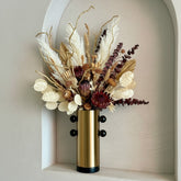 High Objects Orbis Luxe Vase: Cylindrical gold vase with black orb accents, holding a dried floral arrangement.