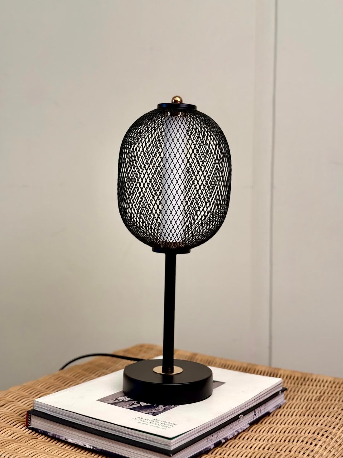 High Objects Orion black mesh pedestal table lamp with gold accent on a round black base, casting a warm glow.