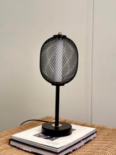 High Objects Orion black mesh pedestal table lamp with gold accent on a round black base, casting a warm glow.
