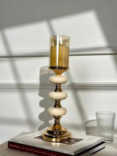 High Objects Pebble Luxe candle stand with amber glass hurricane and tiered pebble-like stem on gold pedestal base.