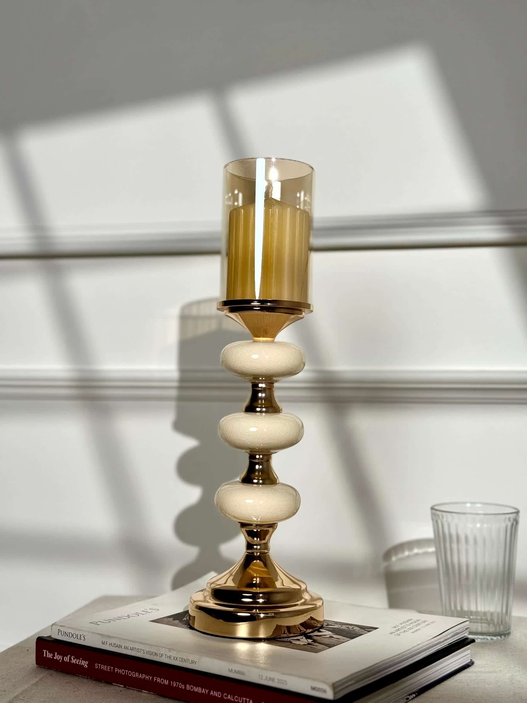 High Objects Pebble Luxe candle stand with amber glass hurricane and tiered pebble-like stem on gold pedestal base.