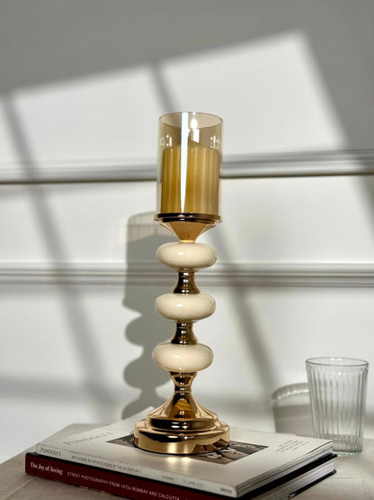 High Objects Pebble Luxe candle stand with amber glass hurricane and tiered pebble-like stem on gold pedestal base.