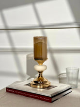 High Objects Pebble Luxe candle stand with gold base, white pebble accent, and amber glass hurricane.