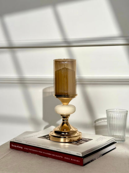 High Objects Pebble Luxe candle stand with gold base, white pebble accent, and amber glass hurricane.