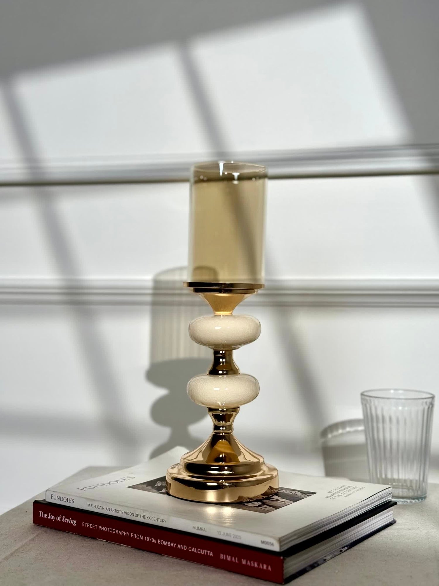 High Objects Pebble Luxe candle stand with gold base, cream pebble-like accents, and amber glass hurricane.