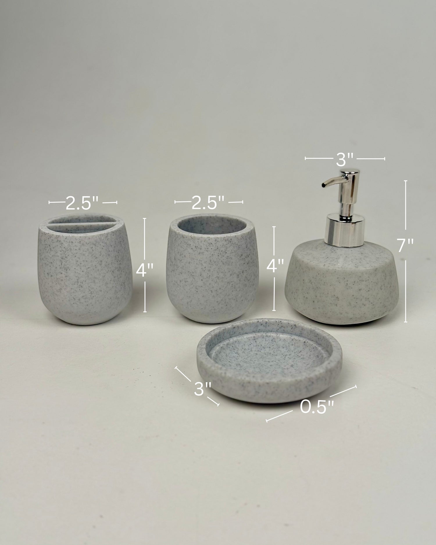 High Objects Pebbleease bathroom accessory set in speckled grey resin, includes soap dish, toothbrush holder, cup, and lotion dispenser.