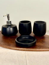 High Objects Pebbleease black bathroom accessory set with soap dispenser, toothbrush holder, and cup on wooden tray.