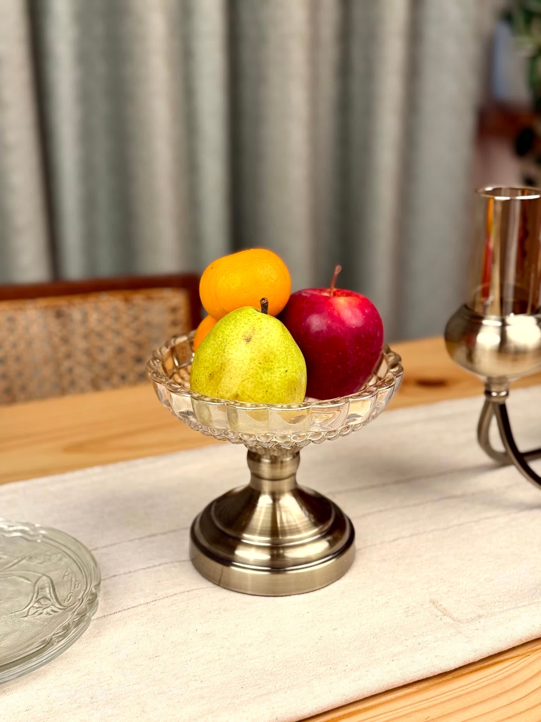 High Objects Crystal Charm Pedestal Bowl, clear glass with scalloped rim, holding fruit on a metallic base.