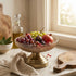 High Objects antique brass pedestal fruit bowl with diamond pattern glass, filled with grapes, figs, pomegranates, and berries.
