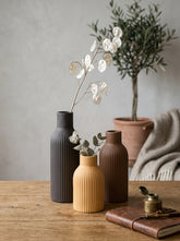 High Objects set of 3 ribbed ceramic vases in black, ochre, and brown. Smallest ochre vase is bulbous, others are tall and slender.