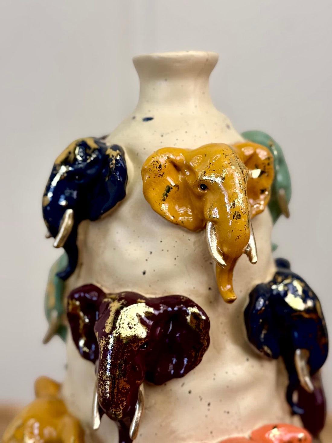 High Objects Safari Heritage Elephant Art Showpiece vase with sculpted elephant heads in blue, yellow, green, and burgundy with gold tusks.