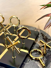 High Objects Sculpted Gold Tic-Tac-Toe Set with gold-finished iron X and O pieces on a black MDF board.